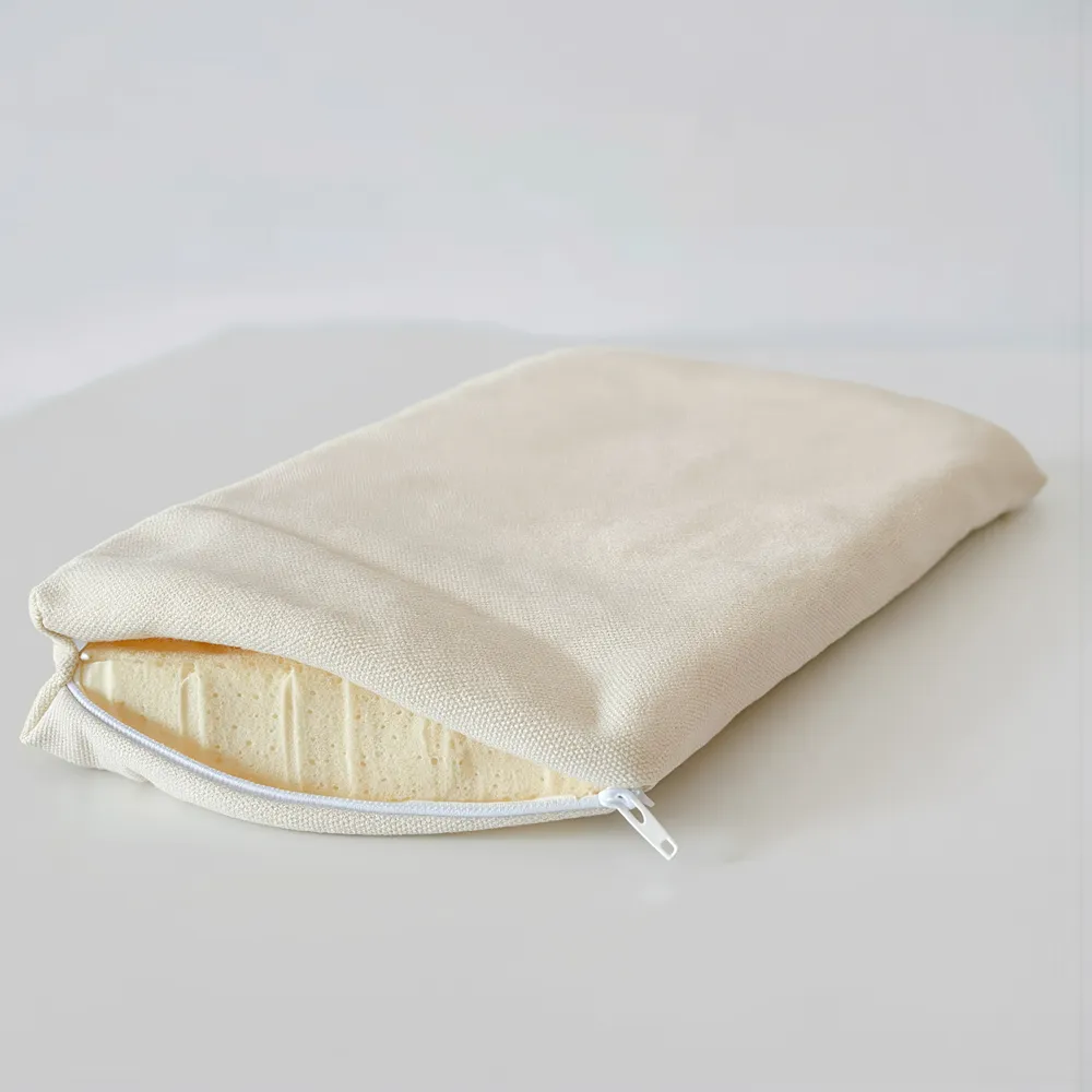 L’alèse zippée en coton écru, posée sur une surface claire, le zip fermé.