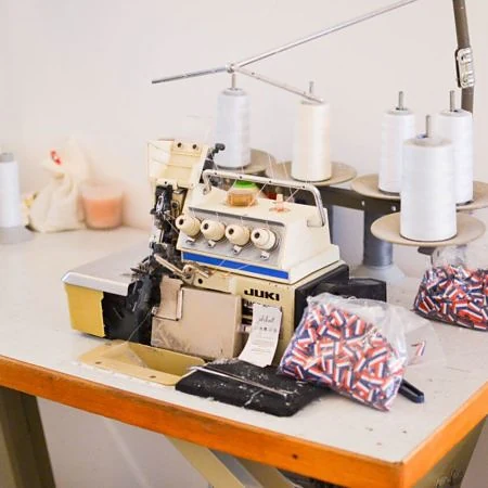 La surjeteuse de l'atelier Jolihuit, bobines de fil blanc et pièces de tissu sur l'établi