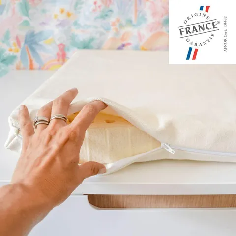 Main qui ouvre l'alèse zippée écrue sur le latex du matelas à langer, logo Origine France Garantie