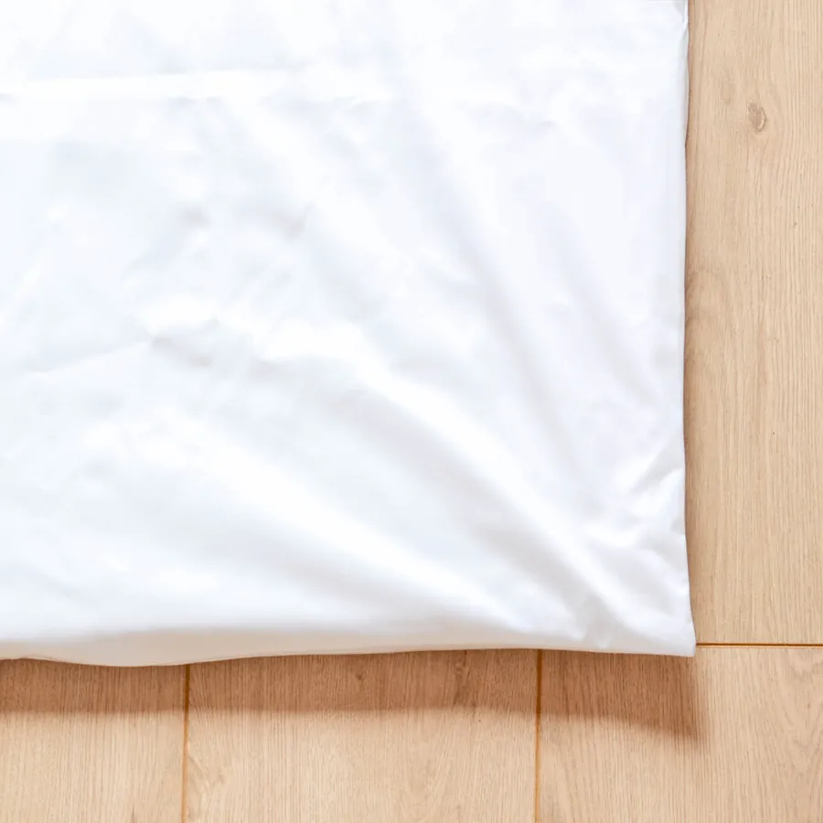 Insert imperméable blanc posé à plat sur un parquet clair, coin replié