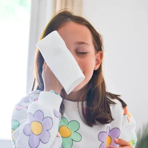 Petite fille les yeux fermés, une lingette lavable posée sur la joue
