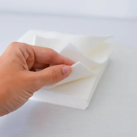 Main qui soulève le coin d'une lingette lavable, fine et souple