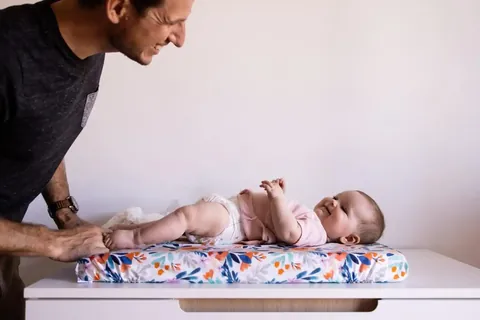 Papa qui change son bébé souriant sur le matelas à langer Bouquet, format paysage