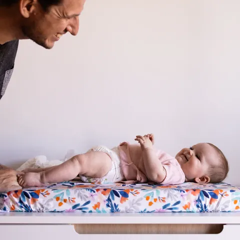 Papa penché sur son bébé allongé sur le matelas à langer Bouquet, tous deux souriants