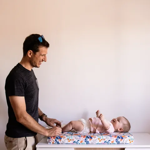 Papa qui change son bébé sur le matelas à langer Bouquet, plan large sur la commode