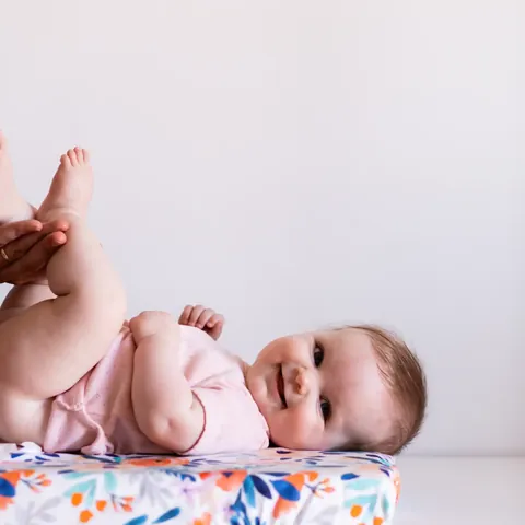 Bébé souriant allongé sur le matelas à langer Bouquet, jambes levées