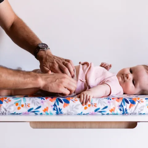 Mains du papa qui ferment la couche du bébé sur le matelas à langer Bouquet