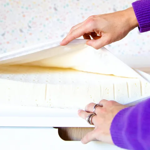 Mains qui soulèvent la housse pour montrer le latex naturel du matelas à langer