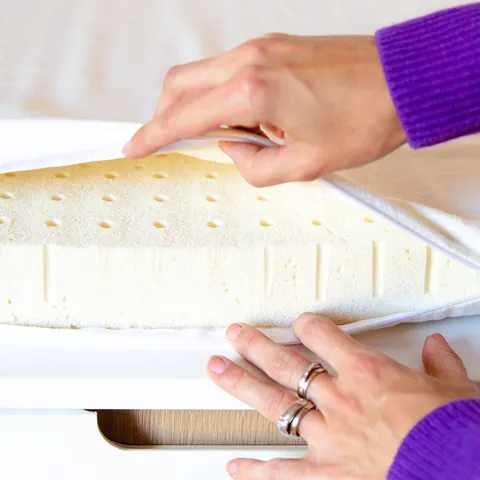 Deux mains soulèvent l'alèse écrue du matelas à langer et découvrent la mousse de latex perforée