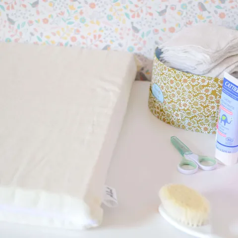 Matelas à langer écru sur la commode, brosse, ciseaux et panière