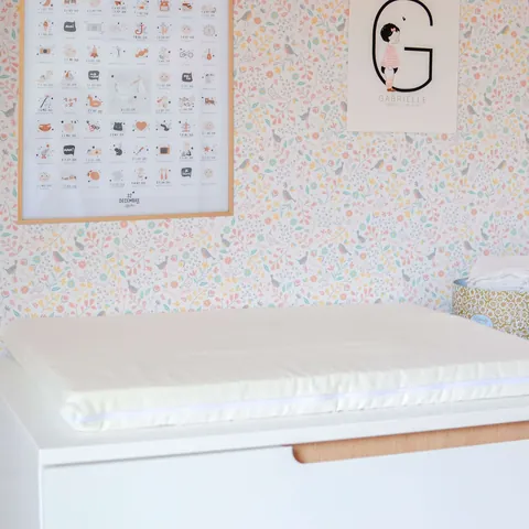 Matelas à langer écru sur la commode, affiche et papier peint fleuri