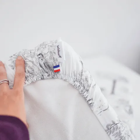 Main qui soulève l'angle de la housse Doux sous-bois, étiquette Jolihuit et drapeau