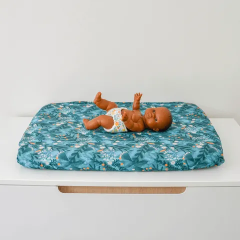 Poupon allongé sur le matelas à langer Forêt magique bleu canard, commode blanche