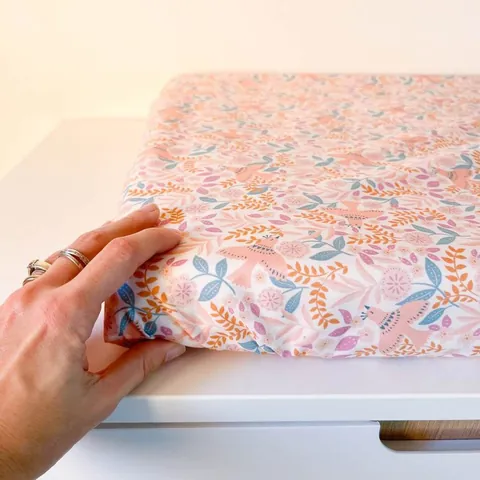 Main posée sur le matelas à langer Poésie, fleurs et feuillages roses et orangés