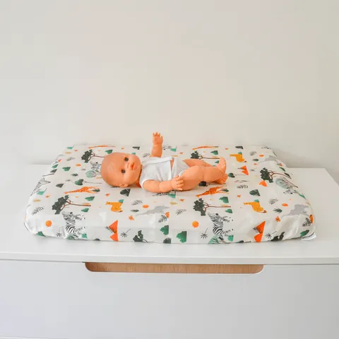 Poupon allongé sur le matelas à langer Savane, girafes et zèbres, commode blanche