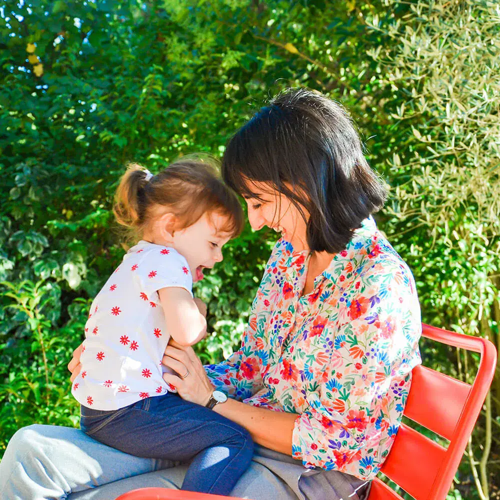 La fondatrice tient sa petite fille dans ses bras, dans un jardin, en robe fleurie