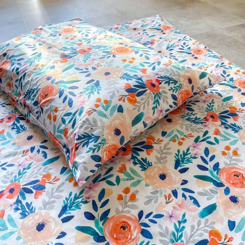 Oreiller housse bouquet posé sur le tapis assorti, grosses fleurs pêche et bleues, gros plan