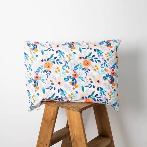 Oreiller housse bouquet posé sur un tabouret en bois, fond blanc