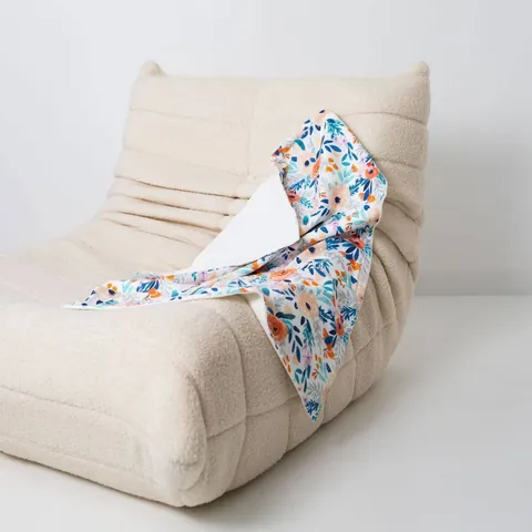 Couverture bouquet drapée sur un fauteuil bas en bouclette écrue, fond blanc