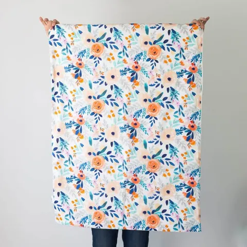 Couverture bouquet dépliée, tenue à bout de bras devant un mur blanc