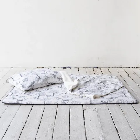 Oreiller et couverture blancs à dessins gris de sous-bois posés sur le tapis assorti, plancher blanc