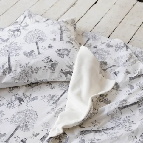 Oreiller, couverture retournée sur sa doublure blanche et tapis à dessins gris de sous-bois, gros plan