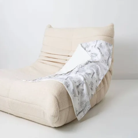 Couverture doux sous-bois drapée sur un fauteuil bas en bouclette écrue