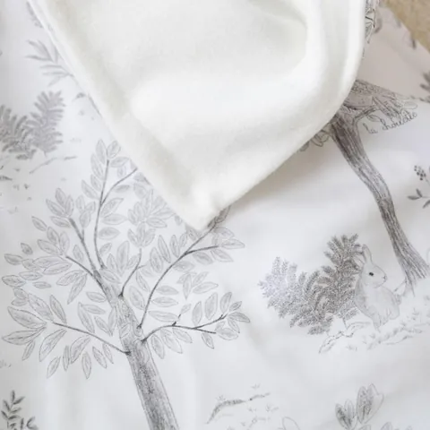 Couverture doux sous-bois et sa doublure blanche, arbres et lapin dessinés, gros plan