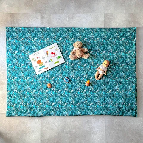 Surhousse géante bleu canard à feuillages étalée au sol, poupon, ours et imagier, vue de dessus