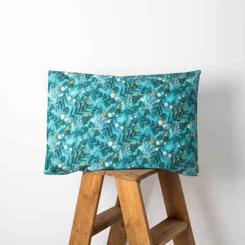 Oreiller housse bleu canard à feuillages posé sur un tabouret en bois, fond blanc