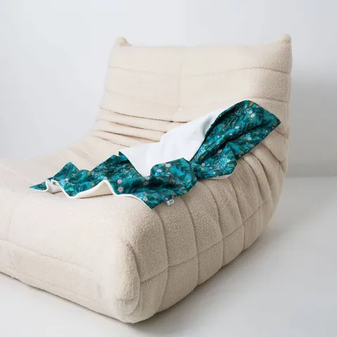 Couverture forêt magique drapée sur un fauteuil bas en bouclette écrue