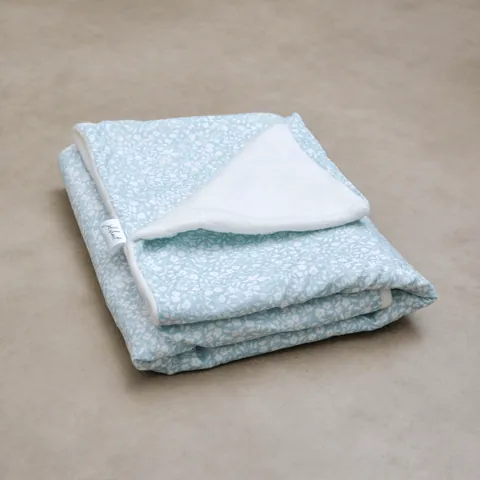 Couverture vert de gris à petites fleurs blanches pliée, coin retourné sur la doublure blanche, sol gris