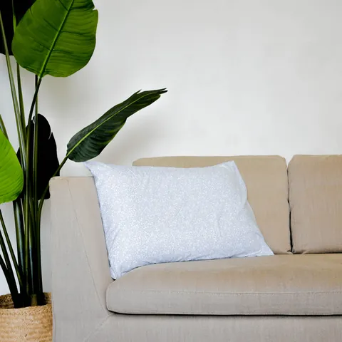 Oreiller housse vert de gris à petites fleurs posé sur un canapé beige, grande plante verte