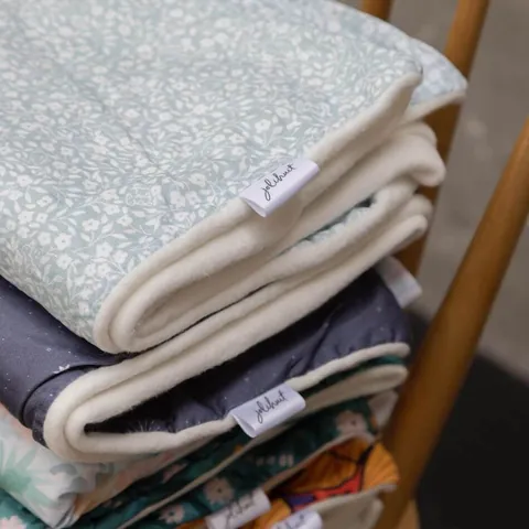 Couverture vert de gris à petites fleurs pliée sur sa doublure blanche, étiquette Jolihuit, gros plan