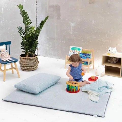 Petite fille qui joue sur le tapis vert de gris avec l'oreiller et la couverture assortis