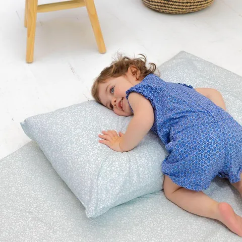 Petite fille allongée en souriant sur l'oreiller vert de gris à petites fleurs, posé sur le tapis assorti