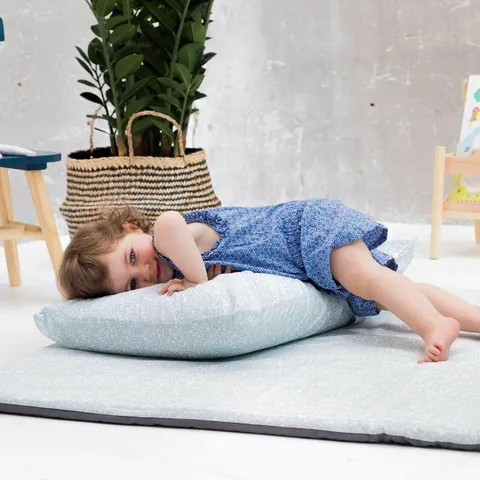 Petite fille allongée sur l'oreiller vert de gris posé sur le tapis assorti, plante et panier