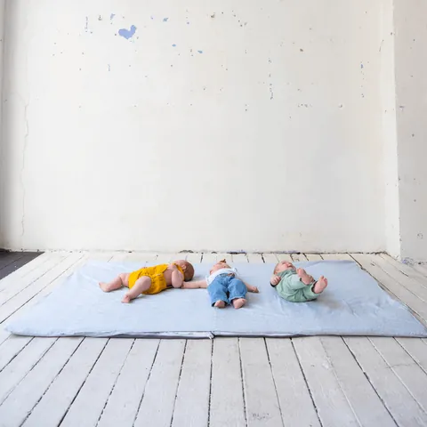 Trois bébés allongés sur la surhousse géante vert de gris, plancher blanc, plan très large