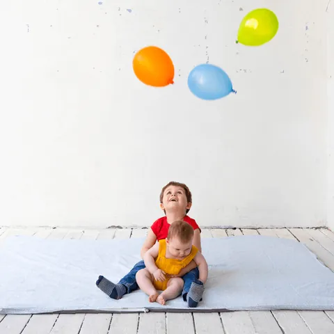 Grand frère et bébé assis sur la surhousse géante vert de gris, ballons colorés en l'air