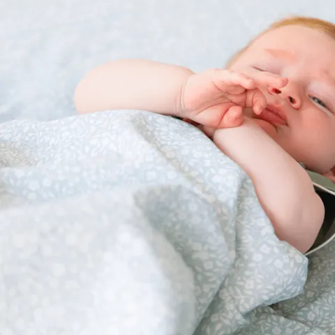 Bébé roux qui se frotte les yeux, couverture vert de gris à petites fleurs au premier plan