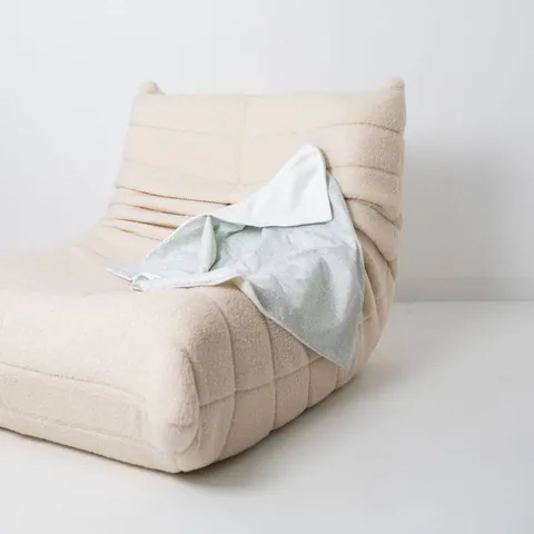 Couverture vert de gris à petites fleurs drapée sur un fauteuil bas en bouclette écrue