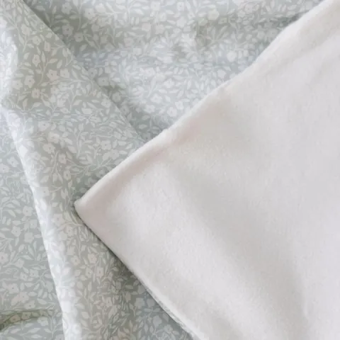 Le coin de la couverture replié, l'imprimé d'un côté et la polaire de coton de l'autre, posé sur un drap clair.