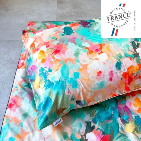 Oreiller housse jardin aux touches de peinture vives posé sur le tapis assorti, logo Origine France Garantie