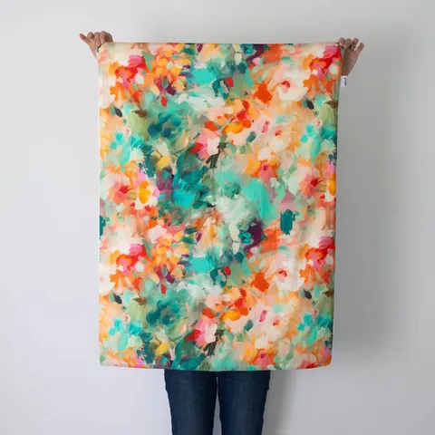 Couverture jardin dépliée, tenue à bout de bras devant un mur blanc