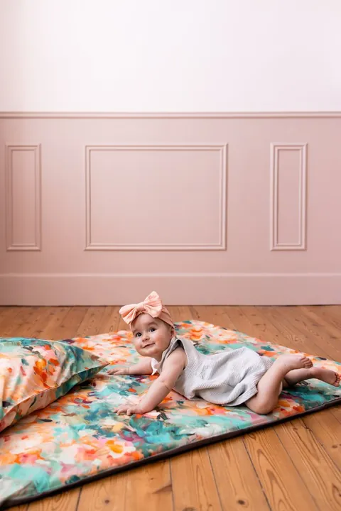 Bébé au noeud rose sur le ventre sur le tapis Jardin, l'oreiller Jardin au premier plan