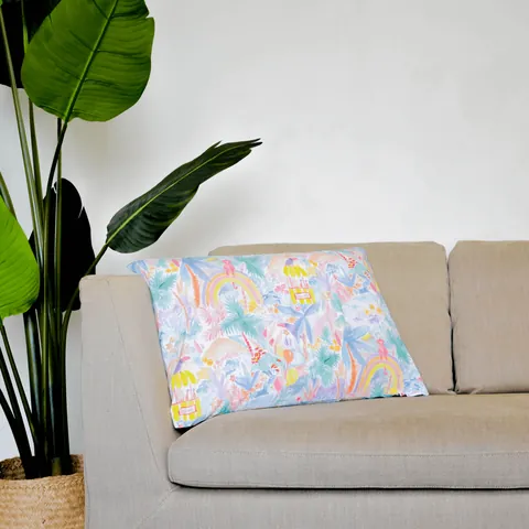 Oreiller housse jungle aquarelle pastel posé sur un canapé beige, grande plante verte