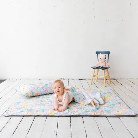 Bébé assis sur le tapis jungle aquarelle avec l'oreiller et la couverture assortis, plancher blanc
