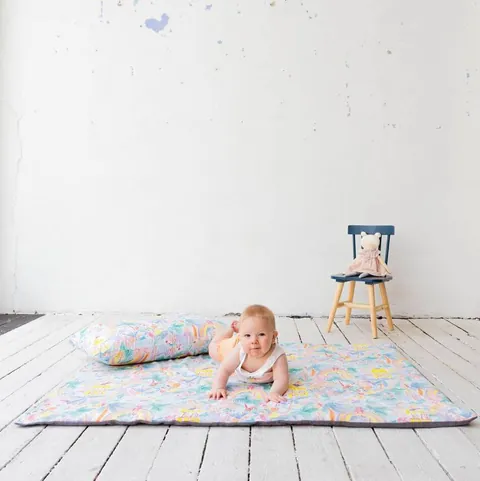 Bébé souriant allongé devant l'oreiller jungle aquarelle posé sur le tapis assorti, plancher blanc