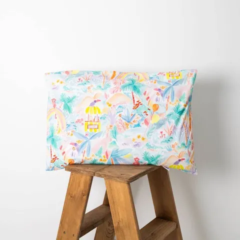 Oreiller housse jungle aquarelle pastel posé sur un tabouret en bois, fond blanc
