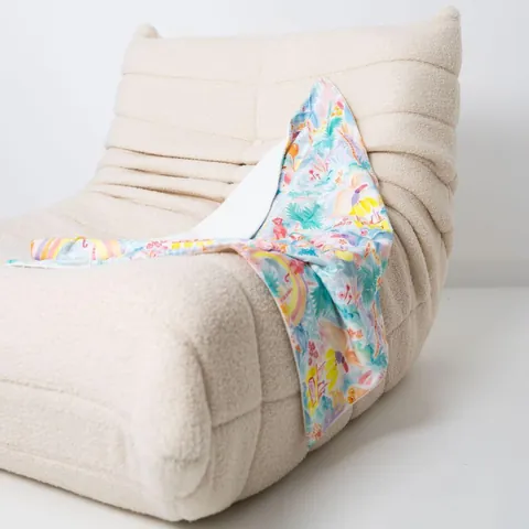 Couverture jungle aquarelle pastel drapée sur un fauteuil bas en bouclette écrue